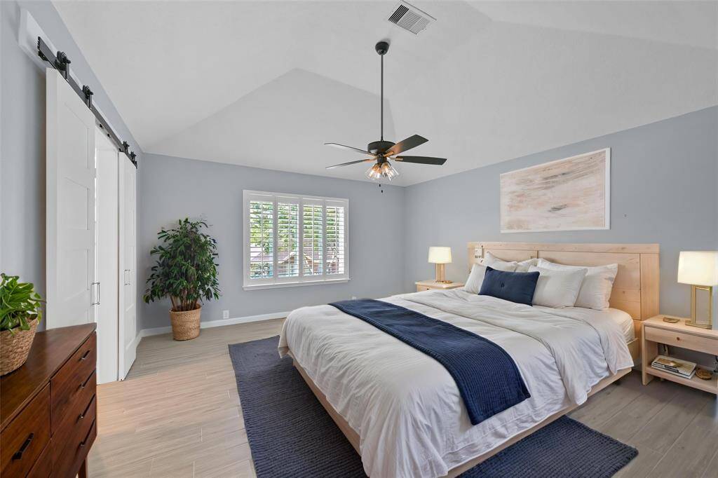 SPACIOUS PRIMARY BEDROOM WITH VAULTED CEILINGS, WOOD-LOOK TILE FLOORING, AND PLANTATION SHUTTERS THAT LET IN TONS OF NATURAL LIGHT. **This room has been virtually staged.