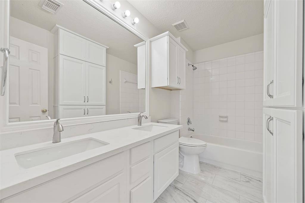 UPDATED BATHROOM FEATURING A NEW COUNTERTOP, MODERN FIXTURES, FRAMED MIRROR, FRESH TOILET, AND ELEGANT TILE FLOORING.