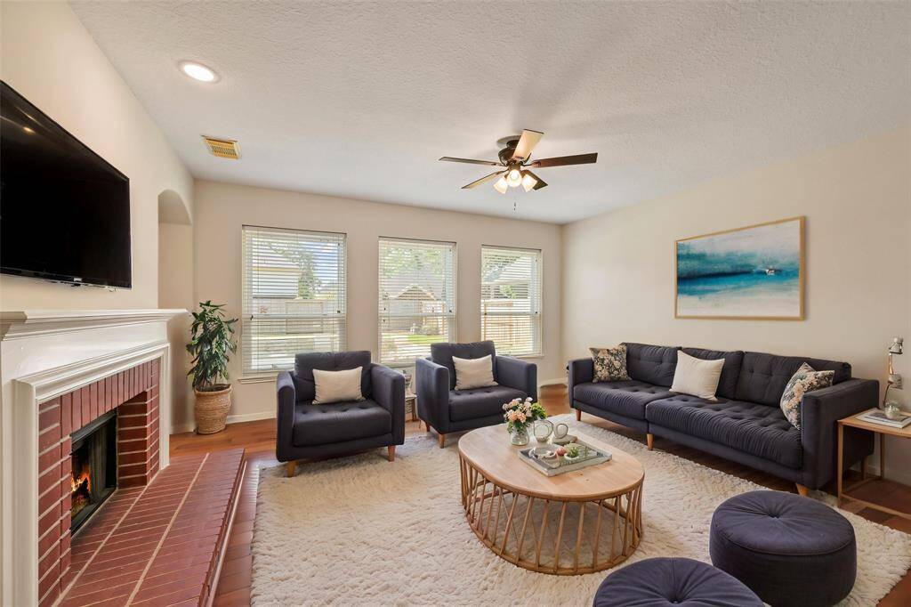 SPACIOUS LIVING ROOM WITH ENGINEERED HARDWOOD FLOORING, A COZY BRICK FIREPLACE, AND LARGE DUAL PANE WINDOWS THAT BRING IN NATURAL LIGHT—FRESHLY UPDATED WITH NEUTRAL INTERIOR PAINT (2025). **This room has been virtually staged.