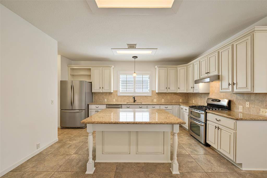 THIS SPACIOUS KITCHEN IS COMPLETE WITH A CENTER ISLAND, STAINLESS APPLIANCES, AND PLANTATION SHUTTER WINDOWS THAT FILL THE SPACE WITH NATURAL LIGHT.