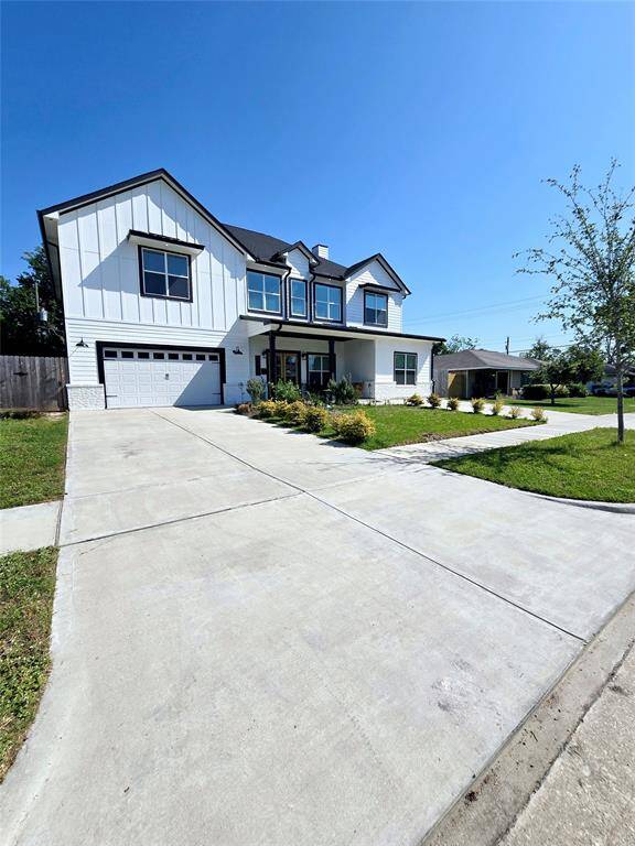 This is a modern two-story home with a white exterior and black trim. It features a double garage, a welcoming front porch, and a well-maintained lawn. The driveway provides ample parking space.