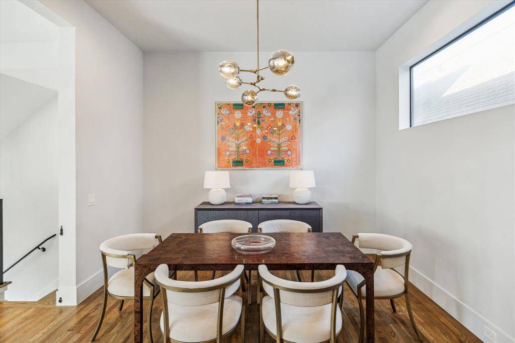 The formal dining room features hardwood floors and is open to both the kitchen and living room, creating an inviting, flowing space. Recessed lighting and a modern designer chandelier illuminate the room, while a window providing northern exposure fills the space with natural light. Neutral designer wall paint enhances the room's elegant, contemporary feel.