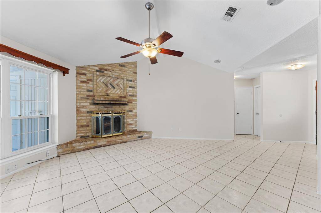 Spacious living room featuring a cozy brick fireplace, elegant tile flooring, and abundant natural light. Perfect for relaxation and entertaining.