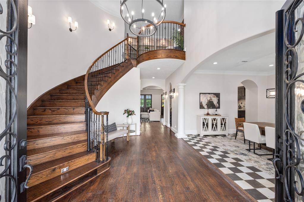 Step into a grand entryway where soaring ceilings create an airy, open feel. A dramatic spiral staircase serves as a stunning architectural focal point, complemented by a statement light fixture that covers the space in a warm, elegant glow.