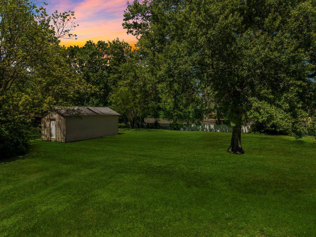 A flat, open terrain framed by mature shade trees and a small storage structure adds both function and charm to this ready-to-develop property.