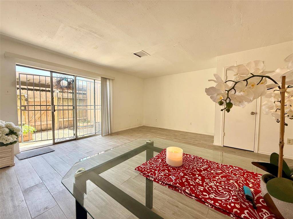 Bright living room with large sliding glass doors leading to a fenced patio. Features neutral tile flooring and a simple, open layout with ample natural light.