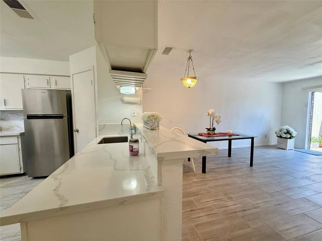 This photo showcases a bright, open-concept kitchen and dining area. The kitchen features modern stainless steel appliances, white cabinetry, and quartz countertops. The dining area is spacious with tile flooring and large windows for natural light.