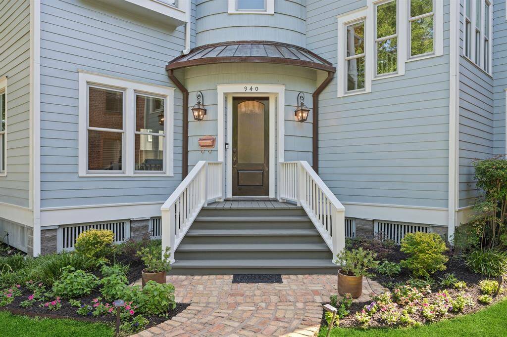 Welcoming front porch, featuring a curved overhang and elegant lanterns. The blue siding is complemented by white trim and the well-maintained garden adds a touch of greenery.