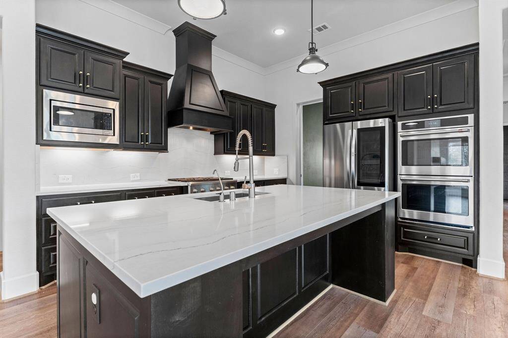The sleek, modern aesthetic is enhanced by rich wood-look vinyl plank flooring, creating a warm yet contemporary ambiance. A generously sized walk-in pantry keeps appliances and essentials neatly tucked away, while the deep, designer sink with an industrial sprayer ensures effortless cleanup. Whether entertaining or enjoying everyday culinary creations, this kitchen is sure to impress.