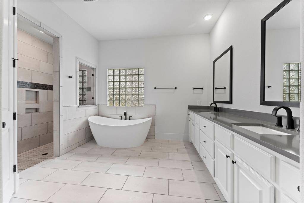 Your Owners’ en suite is a tranquil retreat designed for ultimate relaxation.  The stand-alone vessel soaking tub is the perfect spot to unwind, while the expansive shower offers a refreshing experience. A glass block window allows natural light to filter through, creating a bright and airy ambiance. The custom linen cabinet, dual sinks, and private commode with a Veken bidet system elevate the space to a level of comfort and luxury.
