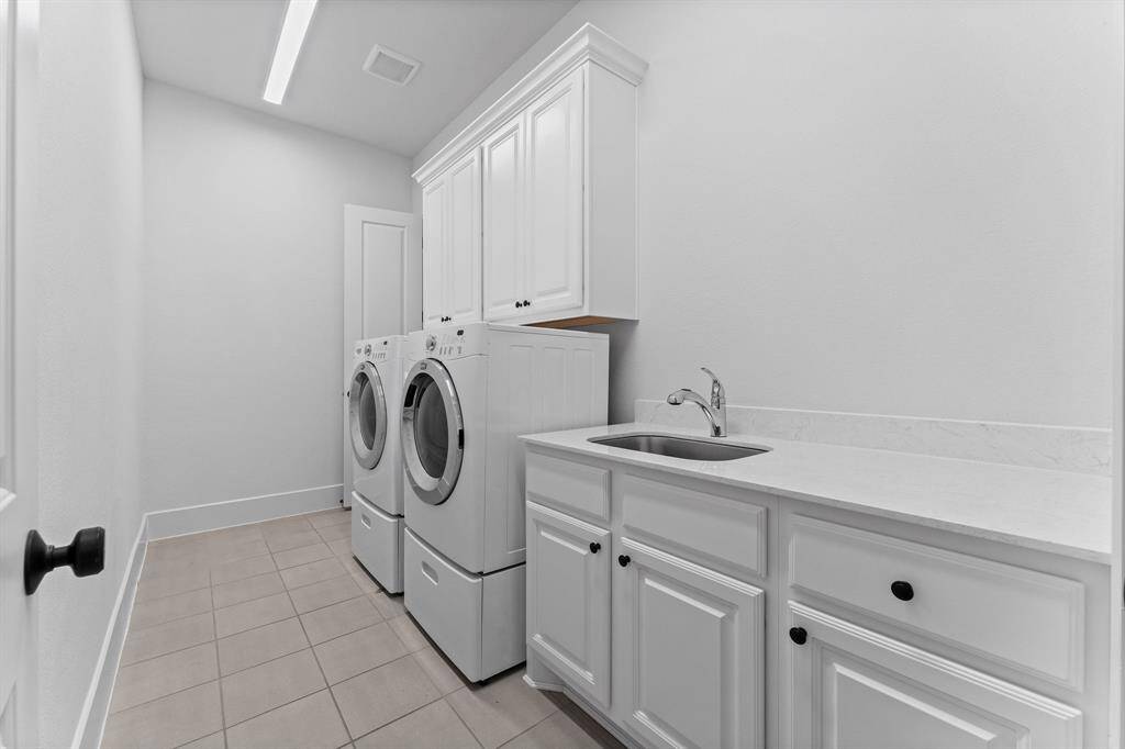 The utility room is thoughtfully located for convenience, with direct access from both the Owner’s suite and the main living areas, making laundry day a breeze. It features durable tile flooring, ample upper and lower cabinetry for storage, and a utility sink with countertop space—perfect for folding clothes and organizing.
