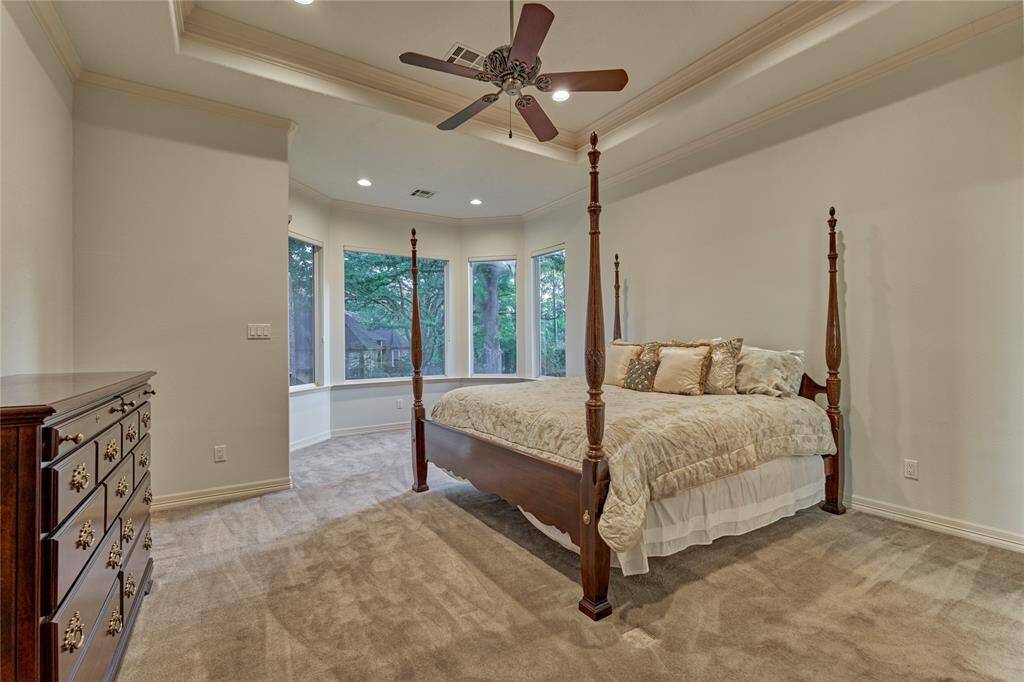 Experience luxury in the private owner's retreat with an elevated tray ceiling, plush carpeting, and a cozy sitting area overlooking serene backyard views.