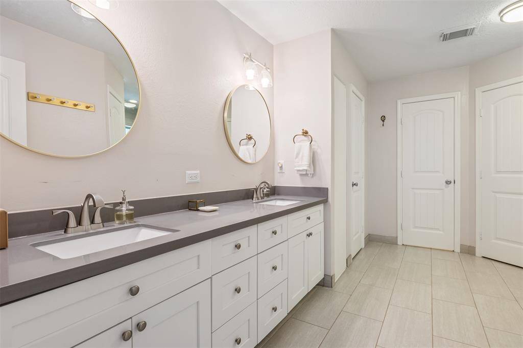 This bathroom has it all with a modern double vanity with sleek gray countertops and round mirrors. The white cabinetry provides ample storage, while soft lighting and neutral flooring create a clean, inviting atmosphere. Not one, and not two but THREE walk in closets.