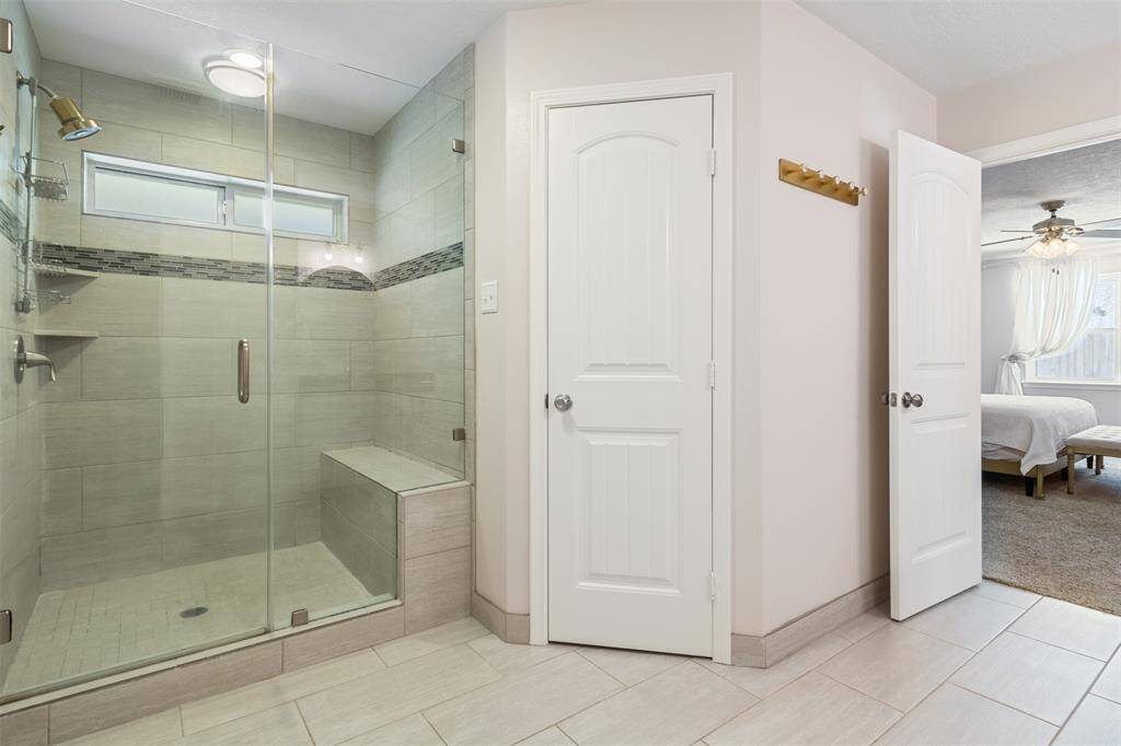 Showcased here is the modern master bathroom with a large walk-in glass shower featuring a built-in bench. The neutral  design is complemented by a decorative strip and a small window for natural light. Adjacent is a door leading to the master bedroom.