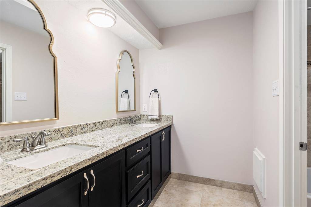 This bathroom features a double-sink vanity with elegant granite countertops and dark cabinetry. The room is well-lit with stylish mirrors and has a clean, modern look.