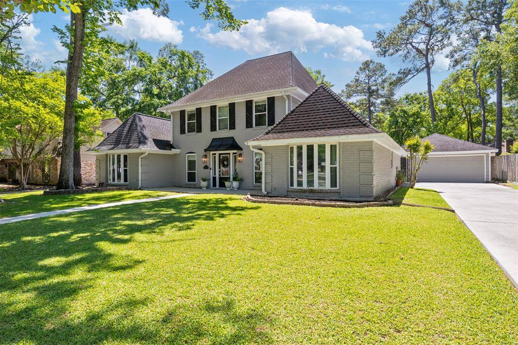 The gorgeous home features a gray exterior with black shutters, a gabled roof, and large front windows. A spacious driveway leads to a detached garage, providing abundance of parking and storage.