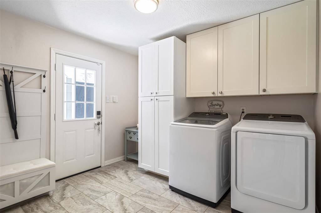 This photo showcases a bright and functional laundry room with modern appliances, ample cabinetry, and a side door for easy outdoor access. The space includes a convenient bench with hooks for storage.