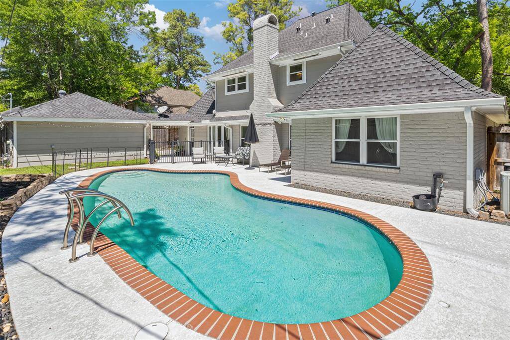 This backyard showcases a unique, curved swimming pool surrounded by a spacious patio. The house features a gray brick exterior, a modern roof, and a cozy backyard perfect for relaxation and entertaining.