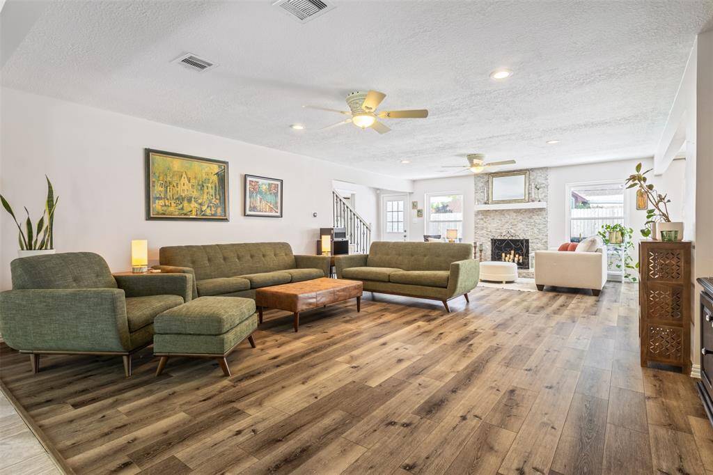 Spacious living room with modern vinyl wood flooring, large windows, and ample natural light. Features include a cozy stone fireplace, custom updated light fixtures and ceiling fans. Ideal for comfortable living and entertaining!