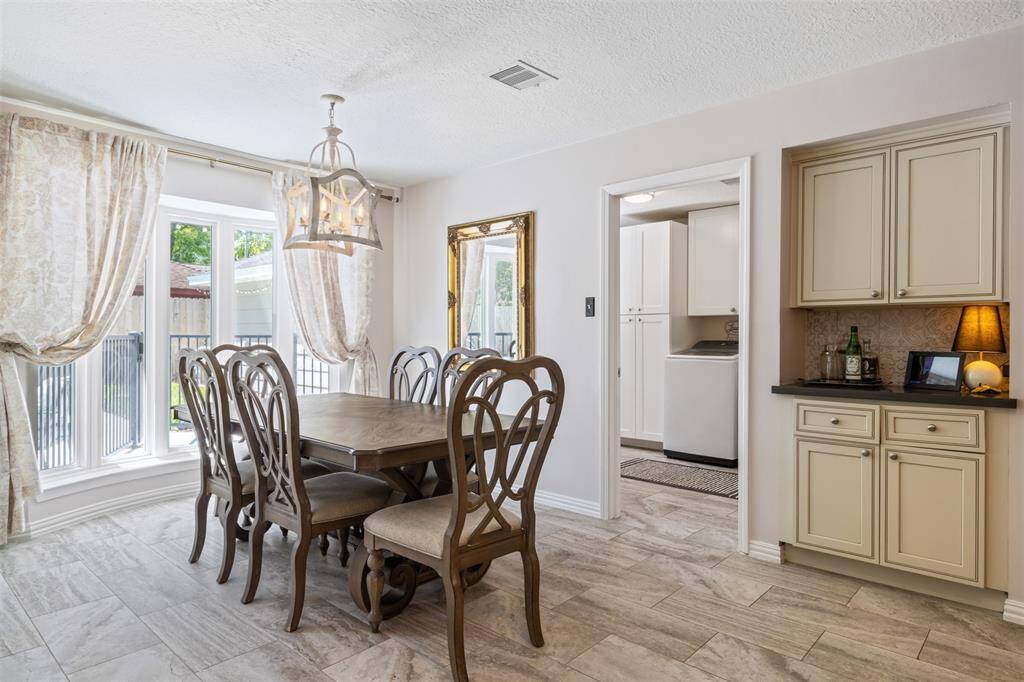 Dining area with lots of natural lighting through the large windows, a stylish chandelier, and custom backsplash at the built in bar area. The room has light-colored flooring and easy access into an adjacent laundry room.