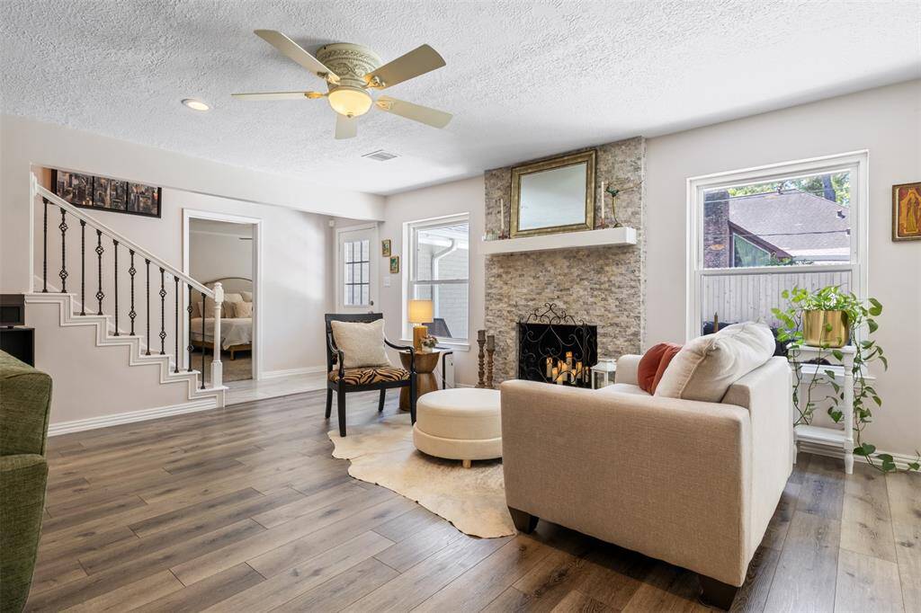 This inviting living room features vinyl flooring, a cozy stone fireplace, and plenty of natural light from two large windows. The space is complemented by neutral colors, a custom ceiling fan, and a stylish staircase leading to the upper level. Perfect for relaxation and entertaining. Additional back door leading to your new backyard oasis!