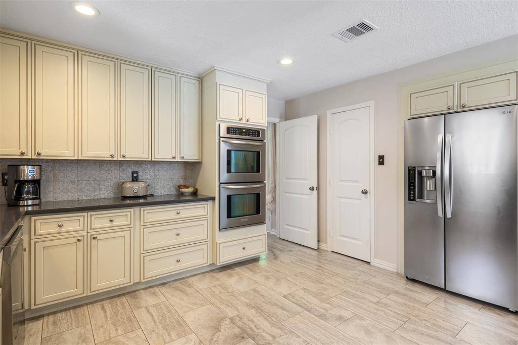 This spacious and versatile kitchen features cream-colored cabinetry, stainless steel appliances including a double oven and fridge, and vinyl flooring.