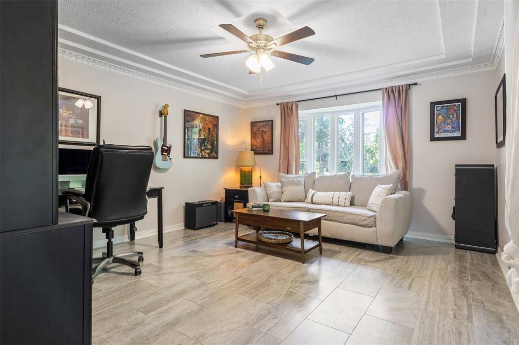 This inviting living room right off the entrance of the home, features gorgeous tile, a ceiling fan, and ample natural light from the large windows. French doors offer a quiet work space and connects to the kitchen.