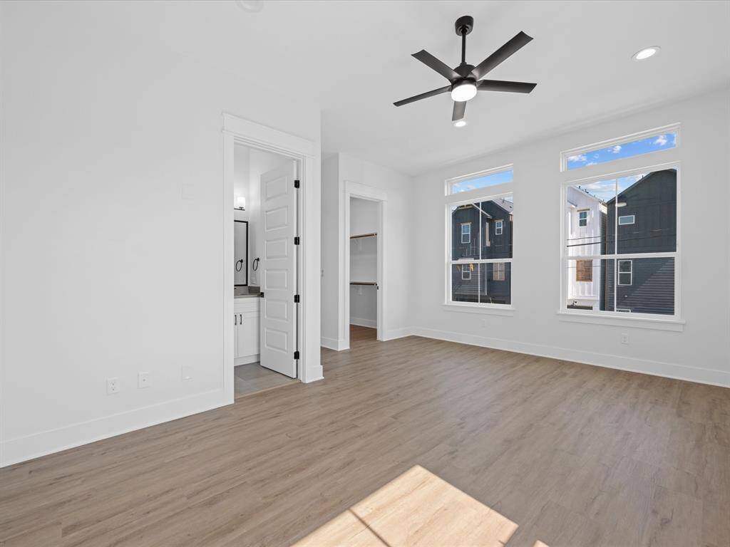 Bright, spacious bedroom with large windows, modern ceiling fan, and wood flooring. Includes a connected bathroom with double sinks and a walk-in closet.