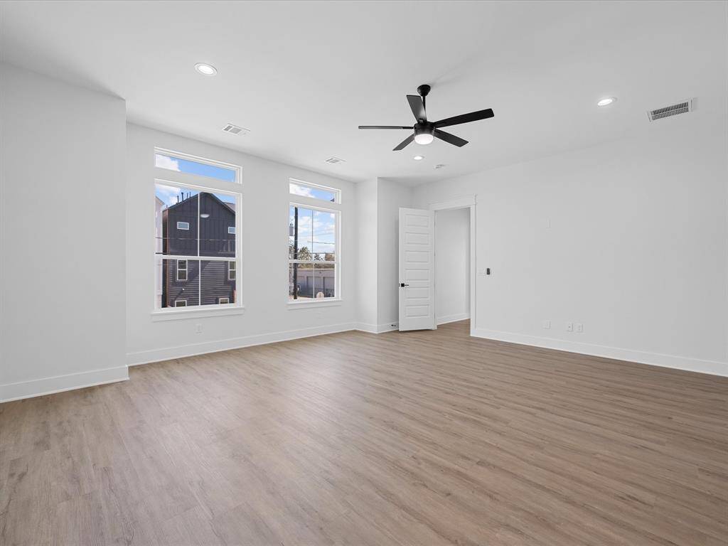 This spacious, bright room features large windows, light wood flooring, and a modern ceiling fan, offering a clean, versatile space ready for personalization.