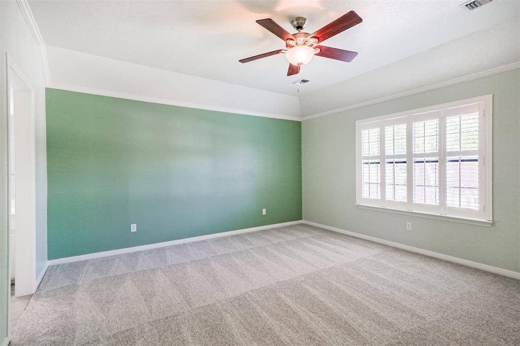 All of the secondary bedrooms are spacious. this one features a green accent wall, tray ceiling , crown molding and plantation shutters.