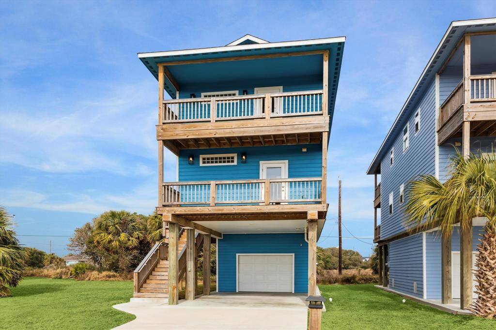 FULLY FURNISHED! You will find it has everything a home needs to move right in. This is a vibrant blue, elevated coastal home featuring a garage and two spacious balconies and a matching set on the back.  All three bedrooms have balconies with incredible views. The home is set against a backdrop of lush greenery and palm trees, offering a serene and tropical atmosphere.
