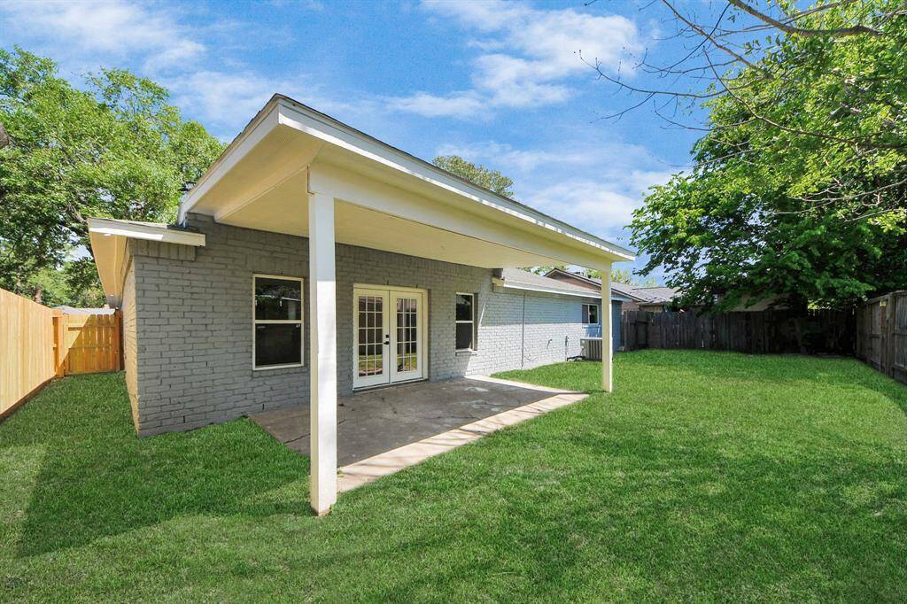 This photo showcases a backyard with a covered patio, perfect for outdoor relaxation. The area features a lush green lawn, wooden fencing for privacy, and is adjacent to a brick house with glass double doors.