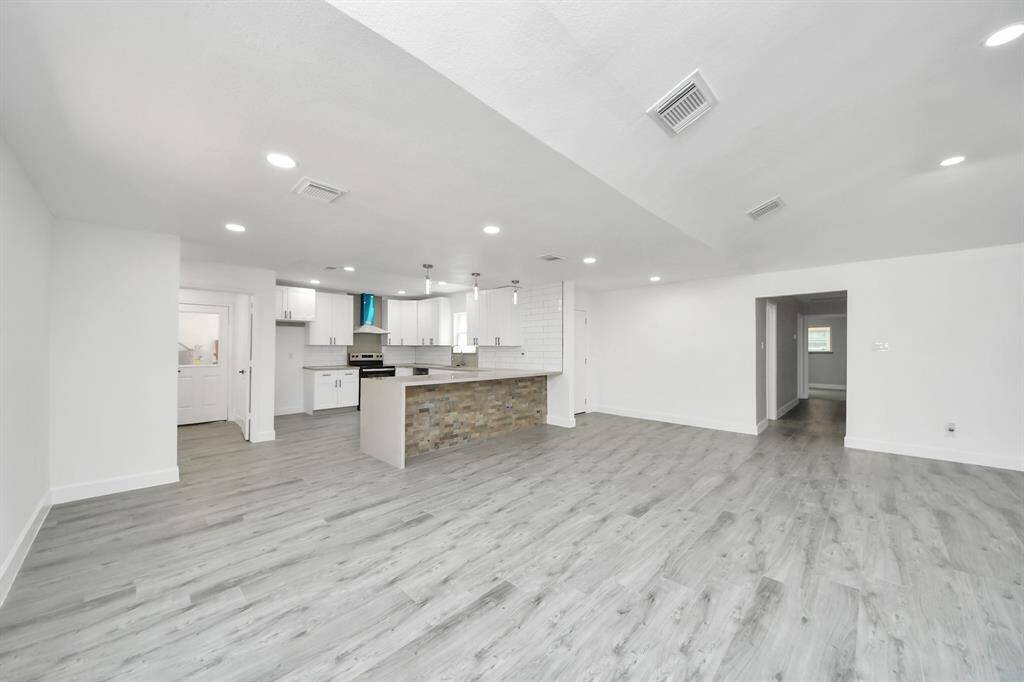 This spacious, open-concept living area features modern finishes with light gray hardwood flooring, recessed lighting, and a sleek kitchen with a stone-accented island. Perfect for entertaining and family gatherings.