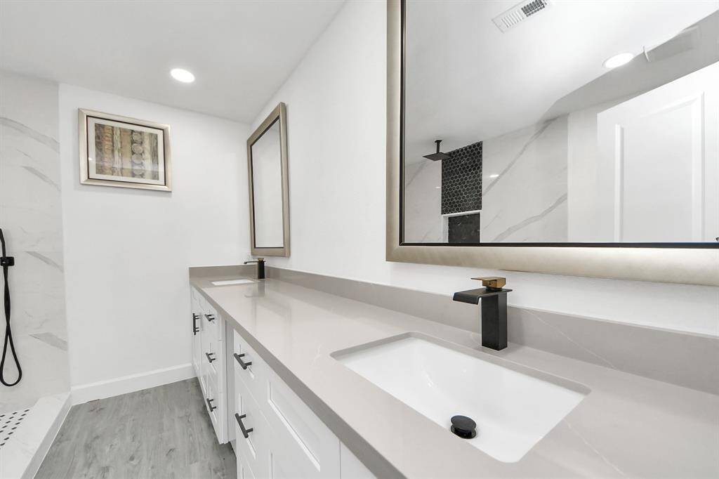 This bathroom features a modern double vanity with sleek black fixtures and large mirrors. It has a clean, white design with ample storage and a walk-in shower, creating a bright and contemporary space.