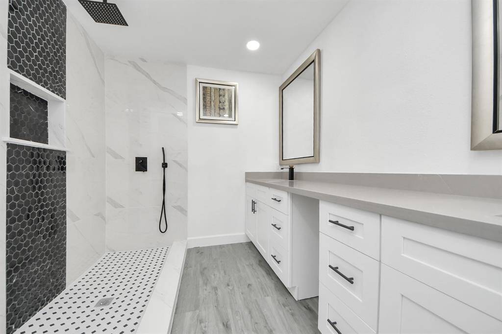 Modern bathroom featuring a spacious walk-in shower with black hexagonal tiles, sleek fixtures, and a long vanity with ample storage and a large mirror. The space is bright with a clean, contemporary design.