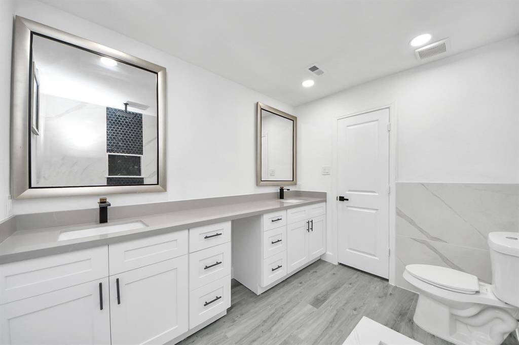 This bathroom features a modern design with dual sinks, sleek white cabinetry, and large mirrors. It has a spacious layout with stylish flooring and a clean, bright ambiance.