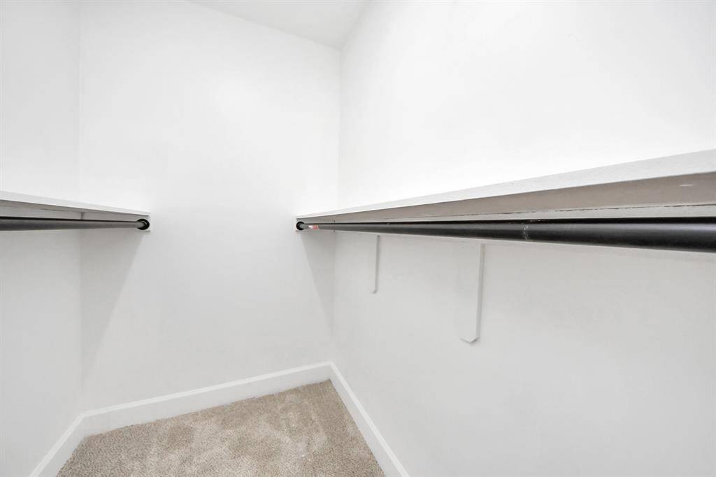 This photo shows a spacious walk-in closet with white walls and dual hanging rods, offering ample storage space. The neutral carpeted floor adds warmth and comfort.