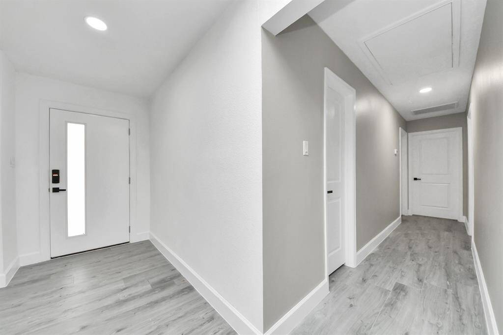 Bright and modern hallway with sleek light gray flooring, neutral walls, and recessed lighting, leading to multiple rooms.