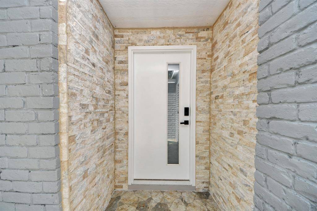 This entrance features a modern white door with a vertical window, surrounded by stylish stone and brick walls, offering a contemporary and welcoming entryway.