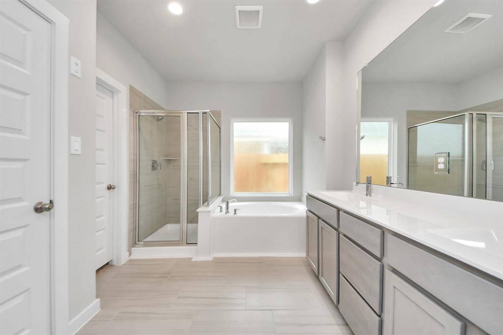 Escape to a spa-like oasis in this primary bathroom. Enjoy a walk-in shower with tile surround, a separate garden tub with custom detailing, and an elegant vanity featuring light countertops, modern hardware, and beautiful recessed lights. Experience luxury and relaxation in every detail. Sample photo of completed home with similar floor plan. Actual colors and selections may vary.