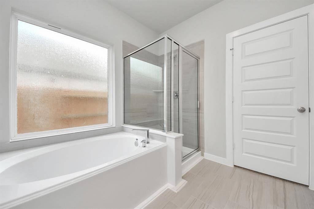 Delight in a spacious walk-in shower enveloped in stylish tile surround and unwind in a separate garden tub adorned with custom detailing. Sample photo of completed home with similar floor plan. Actual colors and selections may vary.
