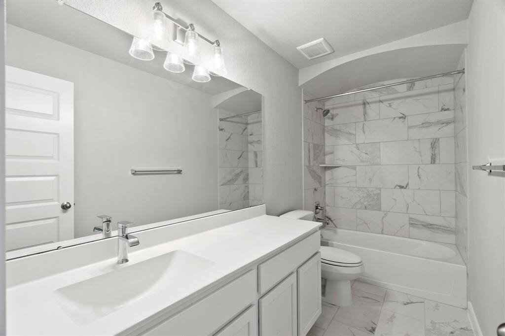 Indulge in refined charm in the secondary bathroom, where the tile flooring harmonizes with a bath/shower combo surrounded by tasteful tile. Light wood cabinets, coupled with a gorgeous countertop, elevate the space, cultivating a truly welcoming atmosphere. Sample photo of completed home. As-built color and selections may vary.