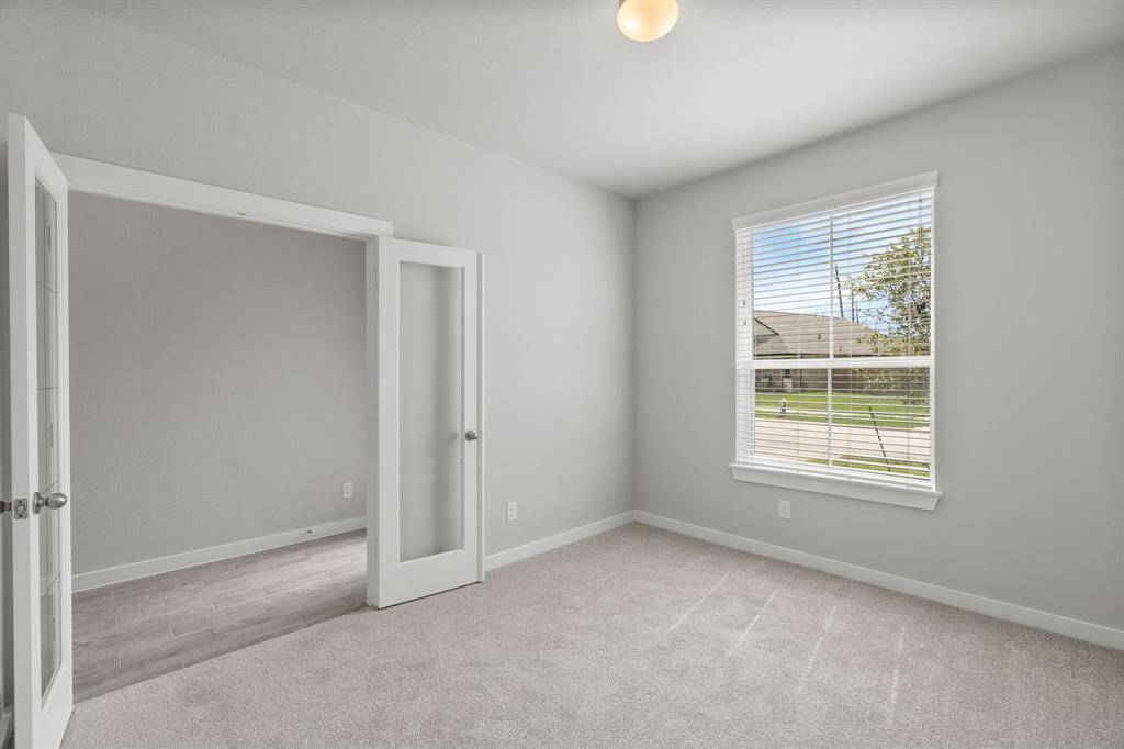 Quietly nestled in front of the home is the sophisticated home office. Featuring plush carpet, custom paint tones, and large windows with privacy blinds. Sample photo of completed home. As-built color and selections may vary.