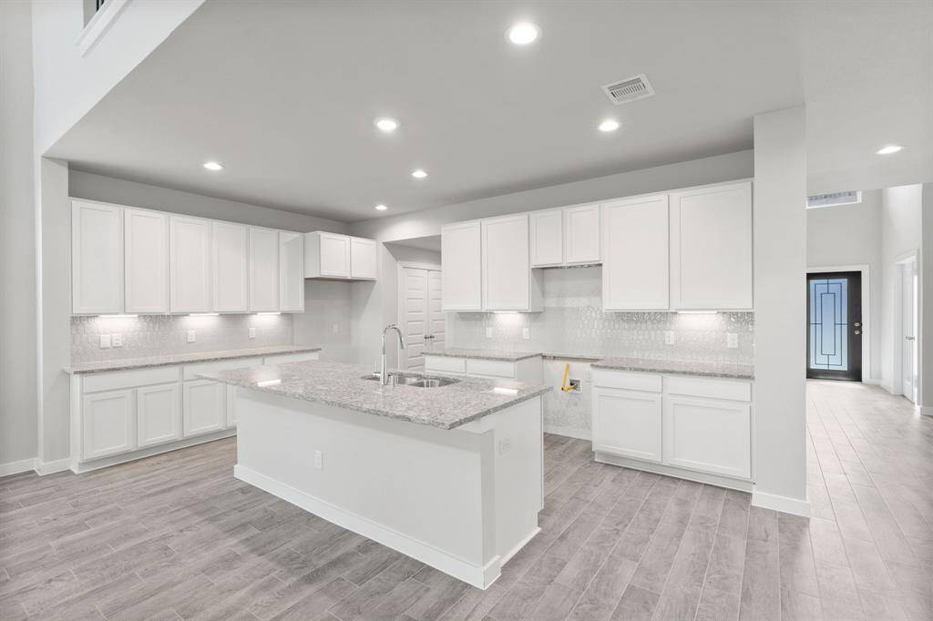 Step into a dream realized with this generously spacious kitchen! A massive granite island takes center stage, complemented by high ceilings, soft-close cabinets, granite countertops, stainless steel appliances, a sleek tile backsplash, and recessed lighting. The extended counter area adds practicality to the stylish design. The open concept effortlessly connects the kitchen to the expansive family room, a perfect hub for gatherings. Sample photo of completed home. As-built color and selections may vary.