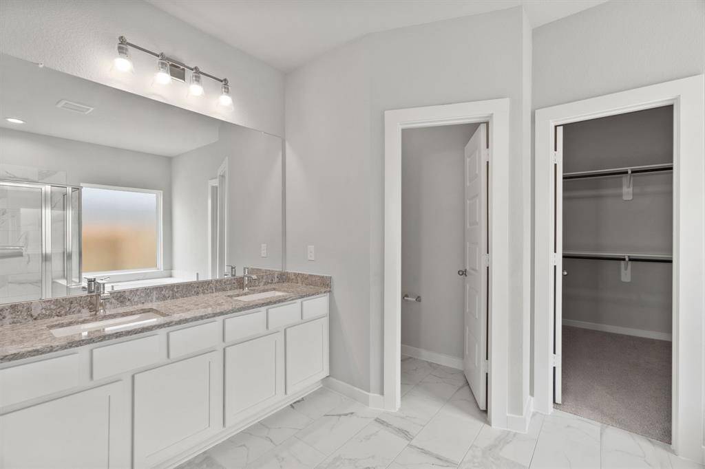 Escape to a spa-like oasis in this primary bathroom. Enjoy a walk-in shower with tile surround, a separate garden tub with custom detailing, and an elegant vanity featuring light countertops, modern hardware, and beautiful vanity lights. Experience luxury and relaxation in every detail. ample photo of completed home. As-built color and selections may vary.