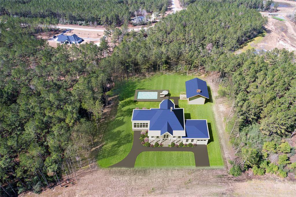 This aerial view showcases a spacious property surrounded by lush forest. The home to be built features a modern design with a blue roof, a large backyard, and a pool. There's also a separate building, likely a garage or guest house, offering additional space. The setting provides privacy and a serene natural environment.