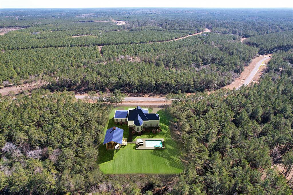 This aerial view showcases a secluded home nestled in a vast forested area, offering privacy and tranquility. The property features a potential to be built spacious house, a separate garage or barn, and a swimming pool, surrounded by lush greenery and expansive woodland. Ideal for nature lovers seeking a peaceful retreat.