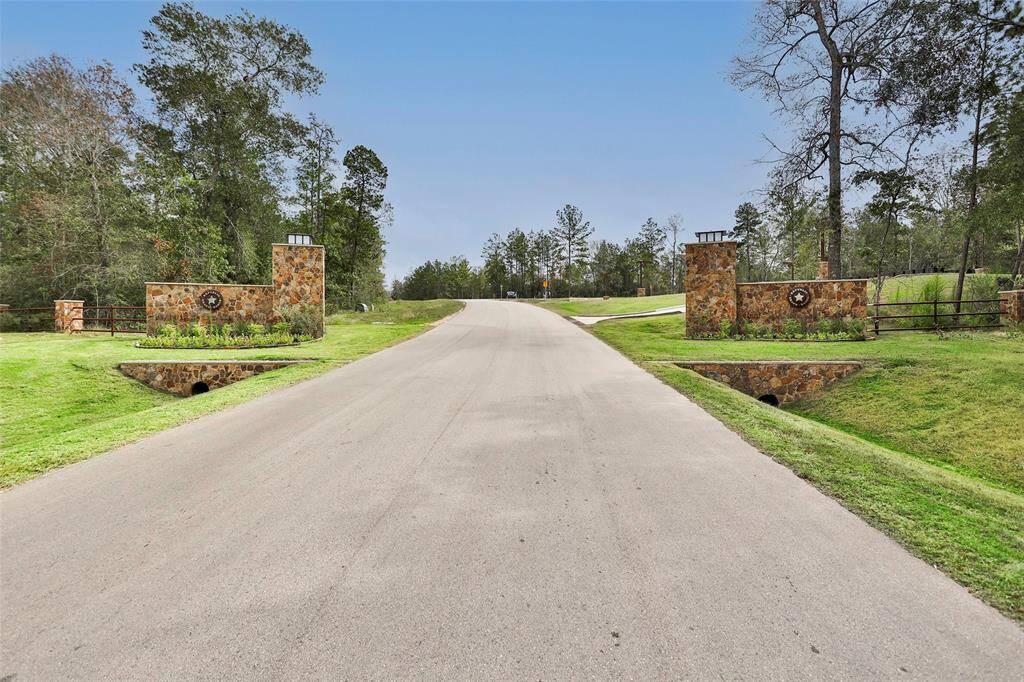 This photo shows a welcoming entrance to a residential community, featuring a paved road flanked by stone pillars and lush greenery, creating a serene and inviting atmosphere.
