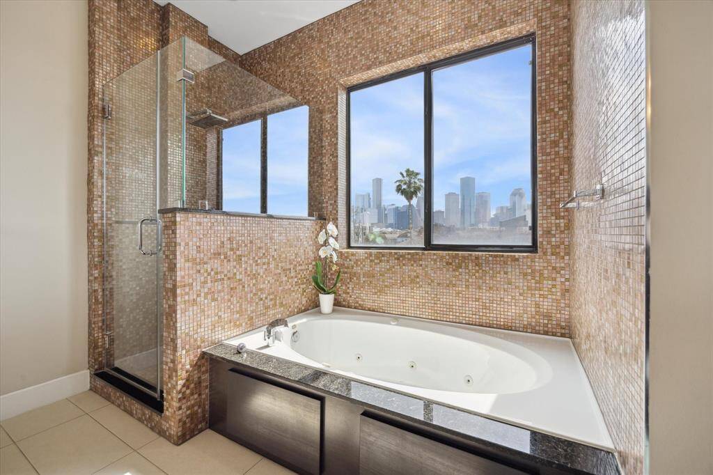 Luxurious primary bathroom showcasing incredible downtown views. Features include glass shower, jetted tub, and mosaic tile work.