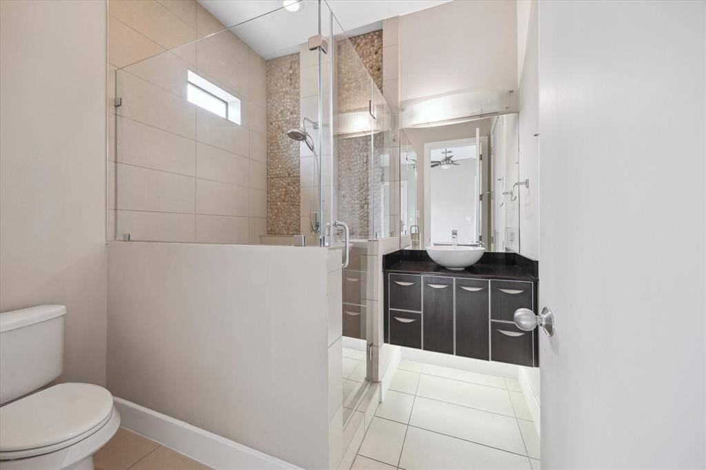 En-suite bathroom features glass shower with mosaic rock wall, white vessel sink, and modern cabinetry.